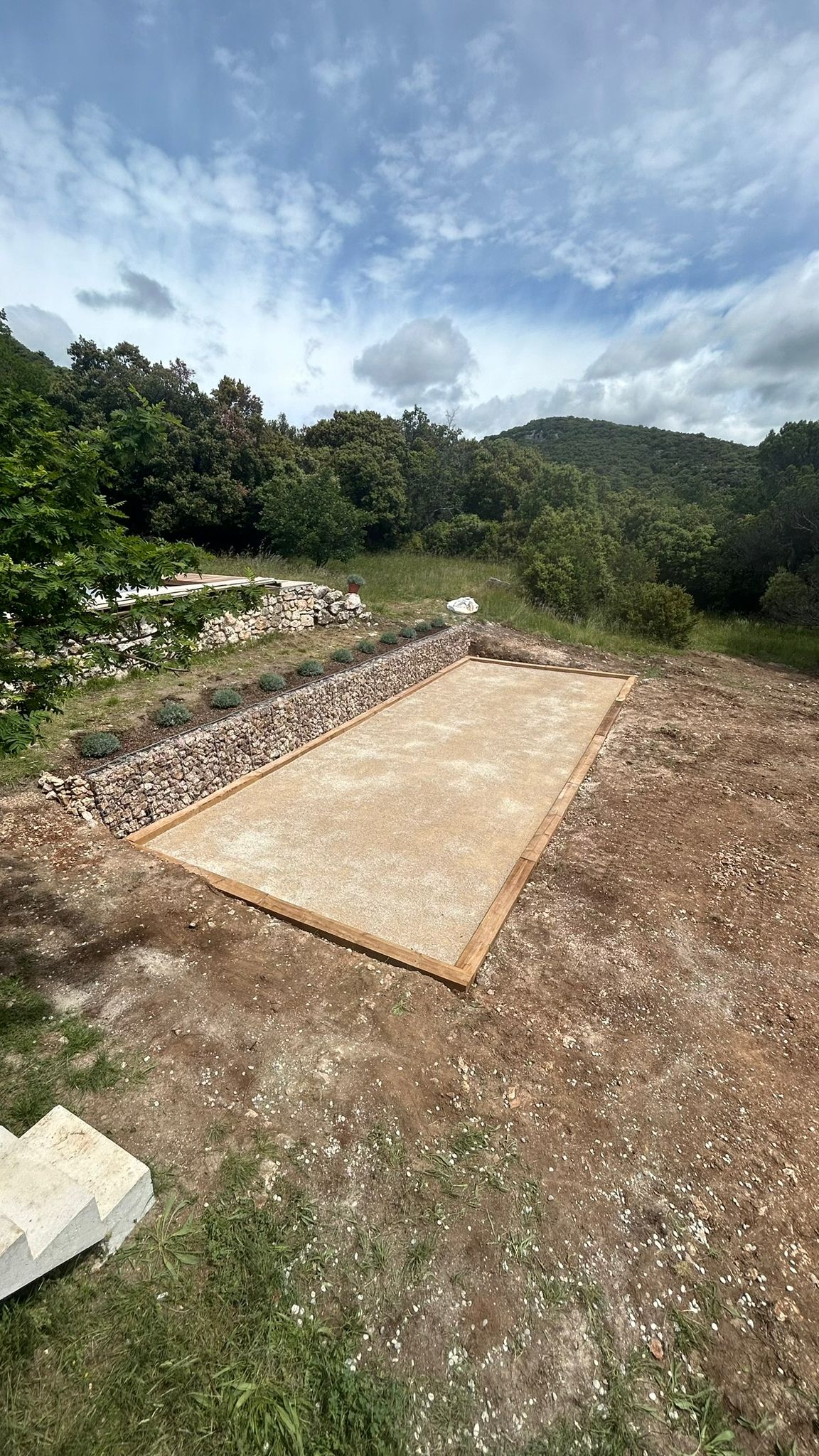 Terrain de pétanque réalisé avec dalle et muret en gabions, vue montagne